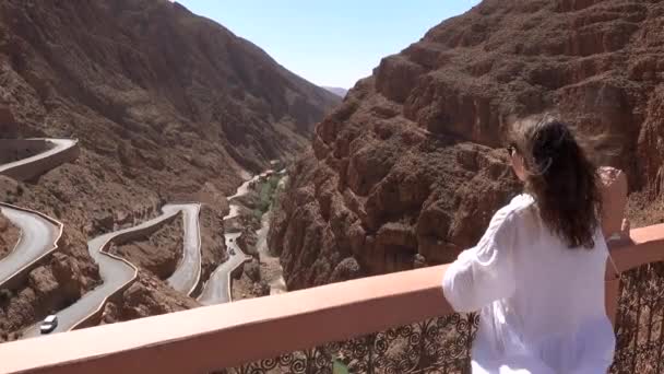 Mujer turista en vestido blanco levantando las manos y disfrutar de la vista de la carretera de montaña ventosa en la garganta de Dades, Gorges Du Dades, Marruecos — Vídeos de Stock