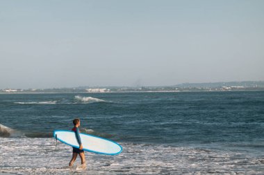 CANGU, BALI, INDONEZYA - 25 Şubat 2019: Mavi sörf tahtası olan sportif adam okyanusta dalgaları yakalamak için suya girer