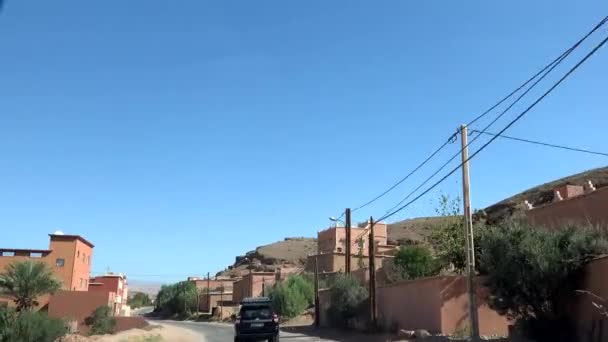 MOROKKO - OKTOBER, 2019: Autofrontansicht auf der Straße mit typischen Lehmhäusern am Straßenrand durch eine kleine marokkanische Stadt in der Nähe von Agadir — Stockvideo