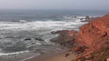 Atlantik Okyanusu manzaralı Fas plajı. Taşlarda ve kırmızı kayalarda dalga vuruşları. Panoramik hava görüntüsü