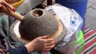 Geleneksel bir şekilde Argan petrol üretimi, Fas. Berber kadının eli kapalı. Sokak pazarının önünde taş aletle fıstık ezmeli makarna yapıyor. 