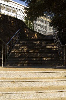 Taş merdiven, demir parmaklık, güneşli gün, ağaçların gölgeleri.