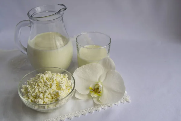 Süt sürahide, süzme peynir cam kasede, beyaz orkide çiçeğinde. Beyaz arka plan. Kahvaltı, basit yemek, günaydın..