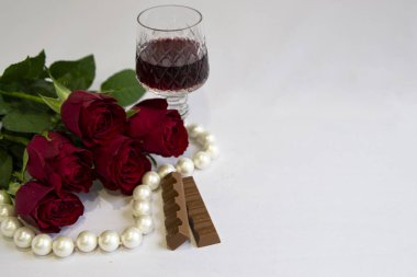 Kırmızı gül buketi, çikolata, bir bardak kırmızı şarap, beyaz arka planda inci, tatil, selamlaşma