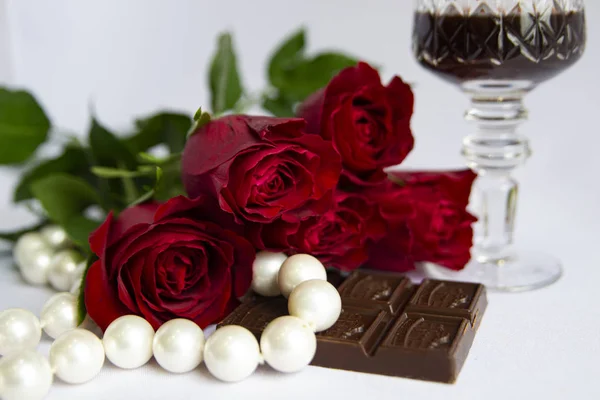 Kırmızı gül buketi, çikolata, bir bardak kırmızı şarap, beyaz arka planda inci, tatil, selamlaşma