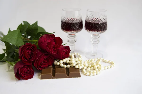 Kırmızı gül buketi, çikolata, bir bardak kırmızı şarap, beyaz arka planda inci, tatil, selamlaşma
