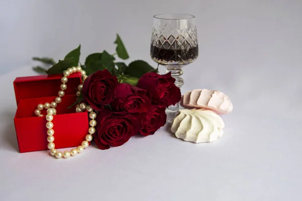 Red roses, pearl beads, glass of red wine, sweets - all on a white background, without anyone