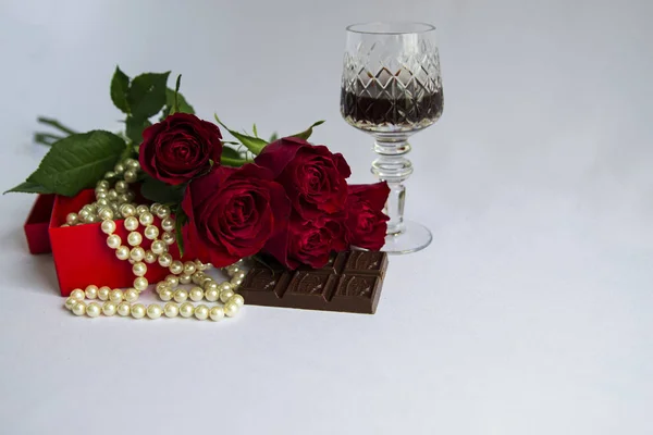 Red roses, pearl beads, glass of red wine, sweets - all on a white background, without anyone