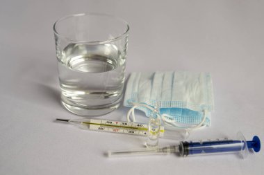 A glass of water, a thermometer with a high temperature indicator, a medical mask, tablets. White background, no one