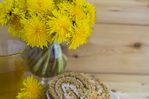Sıcak ahşap arka planda bir buket sarı karahindiba. Cam bardakta bir bardak çay. Kremalı iki dilim bal. Hiç kimse..