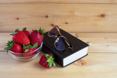 İncil, bardaklar, kırmızı çilekler ahşap bir arka planda vazoda. Sıcak bir ton. Yazıtlar için bir yer var. Günaydın..