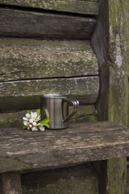 Eski ahşap bir evin duvarına karşı bir bankta duran demir bir bardak su..