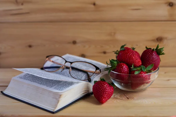 İncil, bardaklar, kırmızı çilekler ahşap bir arka planda vazoda. Sıcak bir ton. Yazıtlar için bir yer var. Günaydın..