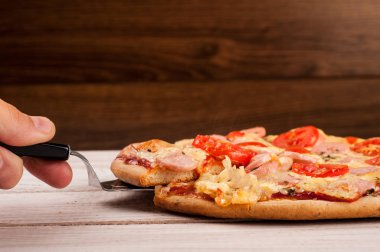 Sıcak pizza dilimi, erimiş peynirle ahşap bir masada.