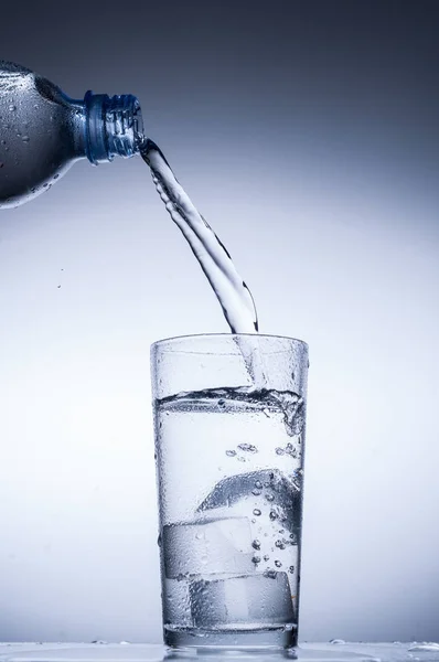 Wasser aus Flasche in Glas auf blauem Hintergrund gießen — Stockfoto