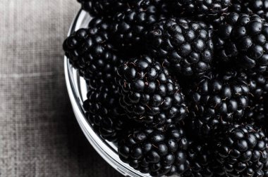 Siyah arka plan üzerine bir tabak içinde olgunlaşmış taze sulu böğürtlen