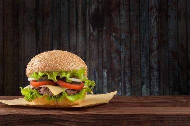 Lezzetli salata malzemelerin üzerine bir ızgara sığır patty boşaltmak bir rustik ahşap masada çizburger