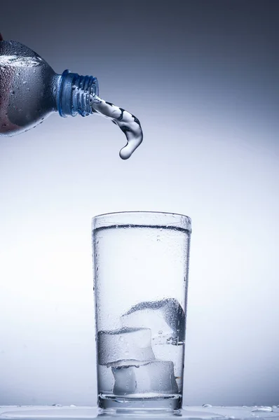 Verter agua de la botella en vidrio sobre fondo azul — Foto de Stock
