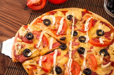 Sıcak pizza dilimi, erimiş peynirle ahşap bir masada.