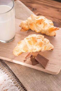 taze pişmiş kruvasanlar bir bardak süt ile ahşap kesme tahtası. Lezzetli kahvaltı