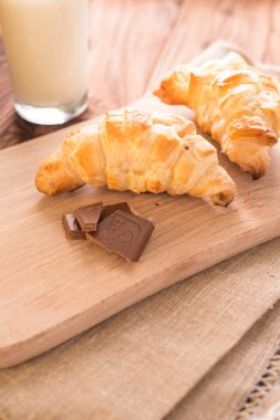 taze pişmiş kruvasanlar bir bardak süt ile ahşap kesme tahtası. Lezzetli kahvaltı
