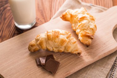 taze pişmiş kruvasanlar bir bardak süt ile ahşap kesme tahtası. Lezzetli kahvaltı