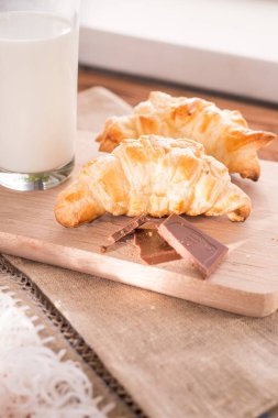 taze pişmiş kruvasanlar bir bardak süt ile ahşap kesme tahtası. Lezzetli kahvaltı