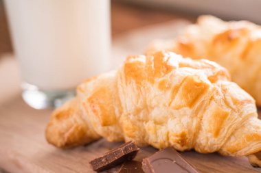 taze pişmiş kruvasanlar bir bardak süt ile ahşap kesme tahtası. Lezzetli kahvaltı