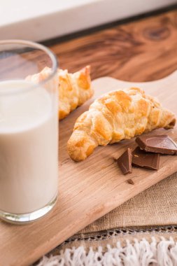 taze pişmiş kruvasanlar bir bardak süt ile ahşap kesme tahtası. Lezzetli kahvaltı