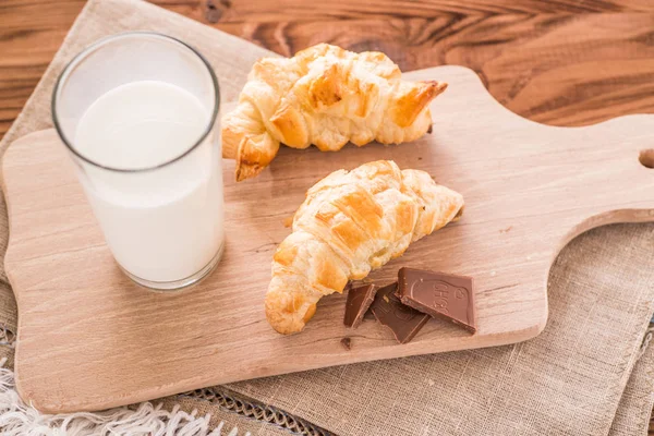 Croissants fraîchement cuits sur une planche à découper en bois avec un verre de lait. Petit déjeuner savoureux — Photo