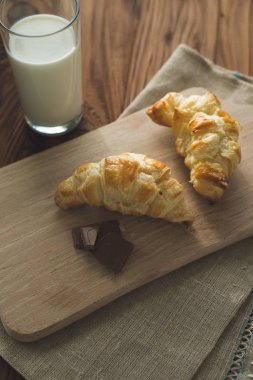 taze pişmiş kruvasanlar bir bardak süt ile ahşap kesme tahtası. Lezzetli kahvaltı