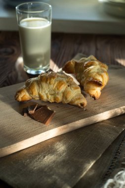taze pişmiş kruvasanlar bir bardak süt ile ahşap kesme tahtası. Lezzetli kahvaltı