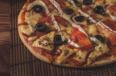 Sıcak pizza dilimi, erimiş peynirle ahşap bir masada.