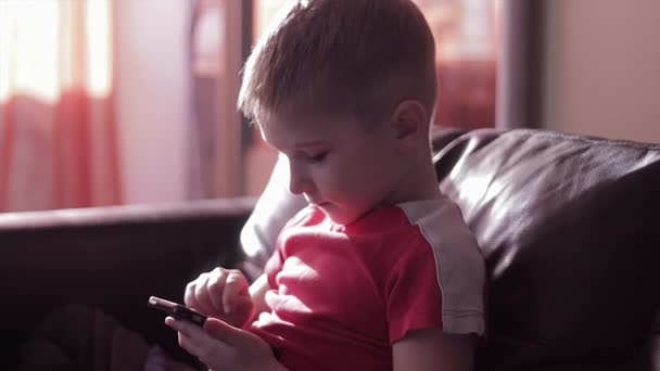 Мальчик играет в игры на смартфоне дома — стоковое видео