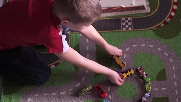 Pequeño chico rubio juega con coches en la alfombra — Vídeo de stock