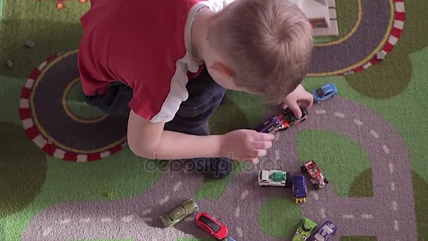 Pequeño chico rubio juega con coches en la alfombra — Vídeo de stock