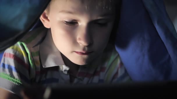 Jongen touchpad liggend onder deken en tekenfilm kijken op — Stockvideo