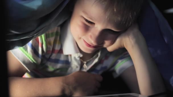 Menino deitado sob cobertor e assistindo desenhos animados no touch pad — Vídeo de Stock