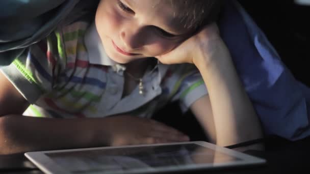 Niño acostado debajo de la manta y viendo dibujos animados en la almohadilla táctil — Vídeos de Stock