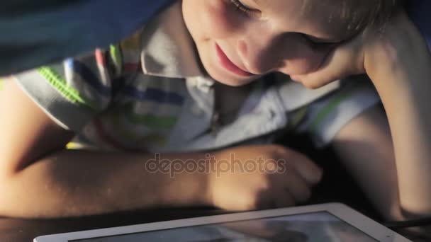 男孩躺在毛毯下并且在上观看卡通触摸板 — 图库视频影像