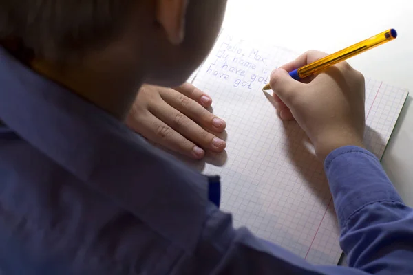 Gros plan de la main d'un garçon avec un crayon écrivant des mots anglais à la main sur du papier pour bloc-notes blanc traditionnel . — Photo