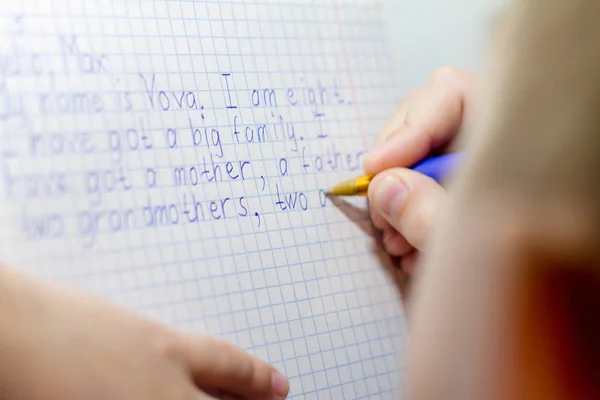 Nahaufnahme einer Jungenhand mit Bleistift, der englische Wörter von Hand auf traditionelles weißes Notizblock-Papier schreibt. — Stockfoto