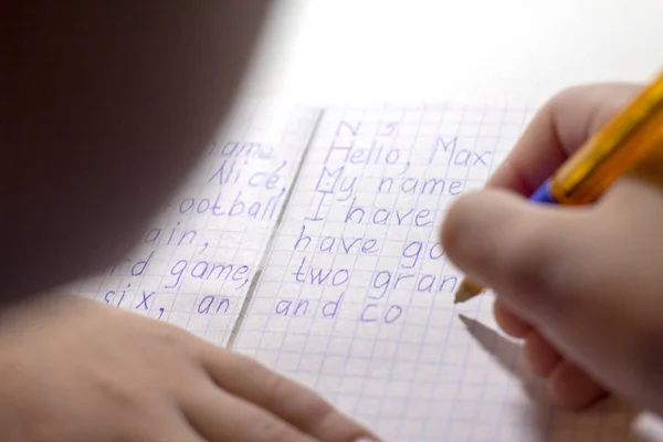 Nahaufnahme einer Jungenhand mit Bleistift, der englische Wörter von Hand auf traditionelles weißes Notizblock-Papier schreibt. — Stockfoto