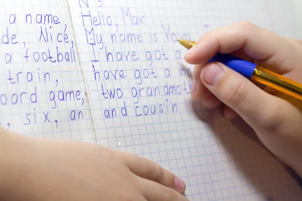 Close-up of boy hand with pencil writing english words by hand on traditional white notepad paper. — Stock Photo, Image