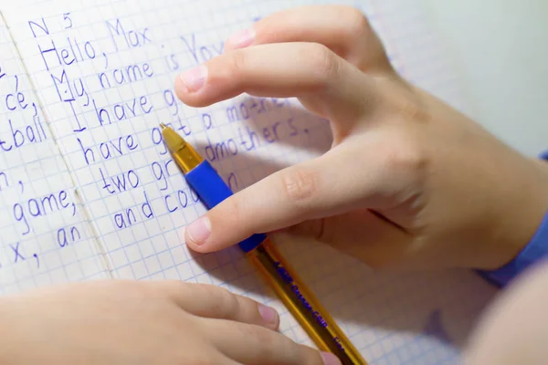 Primer plano de la mano del niño con la escritura a lápiz palabras inglesas a mano en papel de bloc de notas blanco tradicional . —  Fotos de Stock