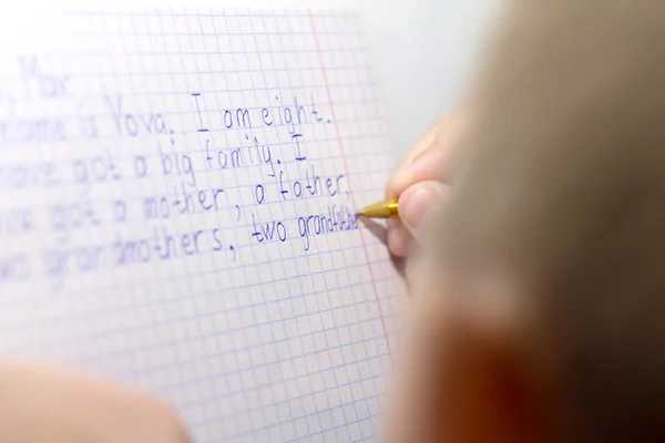 Primer plano de la mano del niño con la escritura a lápiz palabras inglesas a mano en papel de bloc de notas blanco tradicional . —  Fotos de Stock