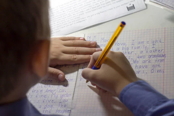 Close-up of boy hand with pencil writing english words by hand on traditional white notepad paper. — Stock Photo, Image