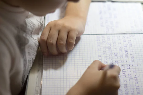 Gros plan de la main d'un garçon avec un crayon écrivant des mots anglais à la main sur du papier pour bloc-notes blanc traditionnel . — Photo