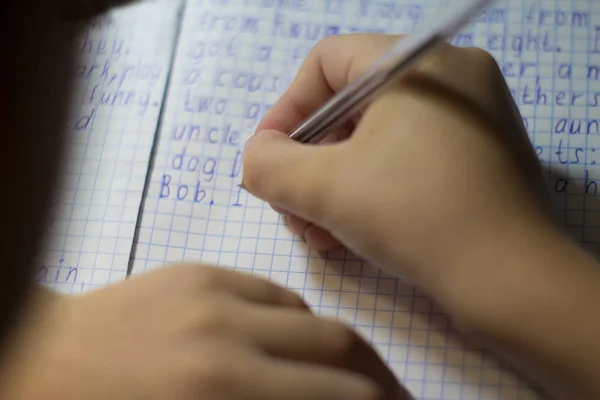 Gros plan de la main d'un garçon avec un crayon écrivant des mots anglais à la main sur du papier pour bloc-notes blanc traditionnel . — Photo