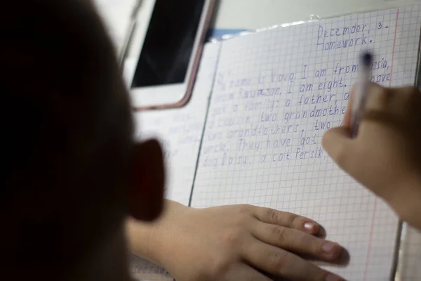 Gros plan de la main d'un garçon avec un crayon écrivant des mots anglais à la main sur du papier pour bloc-notes blanc traditionnel . — Photo